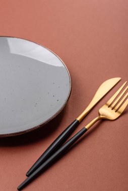 Tek renkli kahverengi arka planda boş seramik plaka. Yemek masasında çatal bıçak takımı olan boş bir tabak.