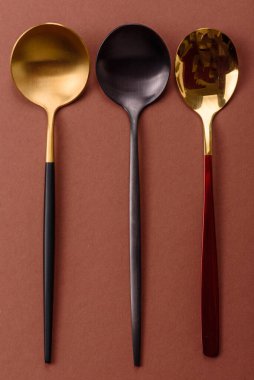 Tek renkli kahverengi arka planda boş metal kaşık. Yemek masasındaki çatal bıçak takımı.