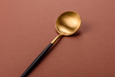 Tek renkli kahverengi arka planda boş metal kaşık. Yemek masasındaki çatal bıçak takımı.