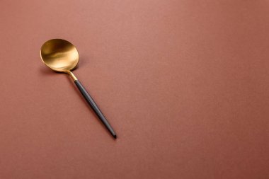 Tek renkli kahverengi arka planda boş metal kaşık. Yemek masasındaki çatal bıçak takımı.