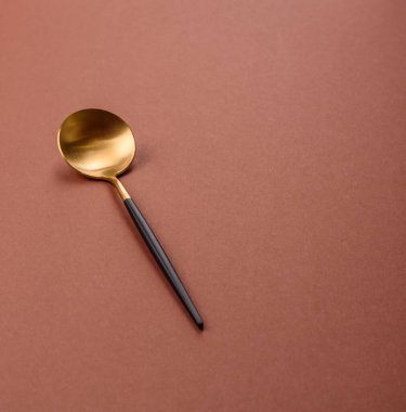 Tek renkli kahverengi arka planda boş metal kaşık. Yemek masasındaki çatal bıçak takımı.