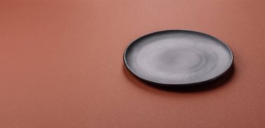 Tek renkli kahverengi arka planda boş seramik plaka. Yemek masasında çatal bıçak takımı olan boş bir tabak.