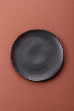Tek renkli kahverengi arka planda boş seramik plaka. Yemek masasında çatal bıçak takımı olan boş bir tabak.
