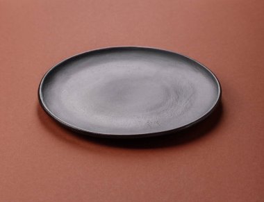 Tek renkli kahverengi arka planda boş seramik plaka. Yemek masasında çatal bıçak takımı olan boş bir tabak.