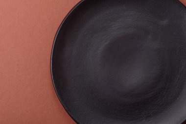 Tek renkli kahverengi arka planda boş seramik plaka. Yemek masasında çatal bıçak takımı olan boş bir tabak.