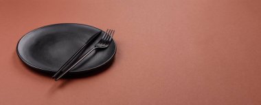 Tek renkli kahverengi arka planda boş seramik plaka. Yemek masasında çatal bıçak takımı olan boş bir tabak.