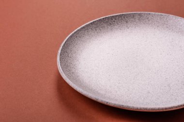 Tek renkli kahverengi arka planda boş seramik plaka. Yemek masasında çatal bıçak takımı olan boş bir tabak.