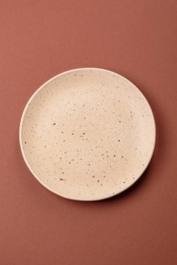 Tek renkli kahverengi arka planda boş seramik plaka. Yemek masasında çatal bıçak takımı olan boş bir tabak.