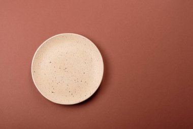 Tek renkli kahverengi arka planda boş seramik plaka. Yemek masasında çatal bıçak takımı olan boş bir tabak.