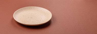 Tek renkli kahverengi arka planda boş seramik plaka. Yemek masasında çatal bıçak takımı olan boş bir tabak.