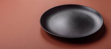 Tek renkli kahverengi arka planda boş seramik plaka. Yemek masasında çatal bıçak takımı olan boş bir tabak.