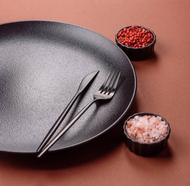 Tek renkli kahverengi arka planda boş seramik plaka. Yemek masasında çatal bıçak takımı olan boş bir tabak.