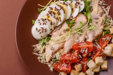 İçinde tavuk, parmesan peyniri, domates, kızarmış ekmek, marul yaprağı, keten tohumu, ayçiçeği ve susam tohumları olan bir kâse dolusu sezar salatası.