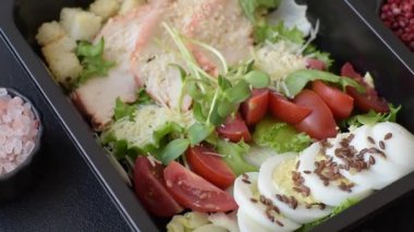 İçinde tavuk, parmesan peyniri, domates, kızarmış ekmek, marul yaprağı, keten tohumu, ayçiçeği ve susam tohumları olan bir kâse dolusu sezar salatası.