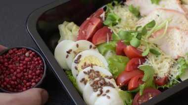 İçinde tavuk, parmesan peyniri, domates, kızarmış ekmek, marul yaprağı, keten tohumu, ayçiçeği ve susam tohumları olan bir kâse dolusu sezar salatası.