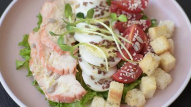 İçinde tavuk, parmesan peyniri, domates, kızarmış ekmek, marul yaprağı, keten tohumu, ayçiçeği ve susam tohumları olan bir kâse dolusu sezar salatası.