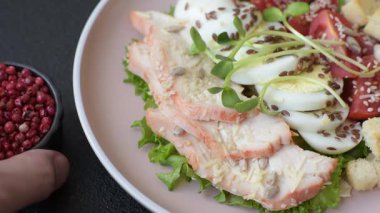 İçinde tavuk, parmesan peyniri, domates, kızarmış ekmek, marul yaprağı, keten tohumu, ayçiçeği ve susam tohumları olan bir kâse dolusu sezar salatası.