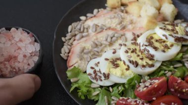 İçinde tavuk, parmesan peyniri, domates, kızarmış ekmek, marul yaprağı, keten tohumu, ayçiçeği ve susam tohumları olan bir kâse dolusu sezar salatası.