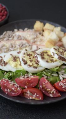 İçinde tavuk, parmesan peyniri, domates, kızarmış ekmek, marul yaprağı, keten tohumu, ayçiçeği ve susam tohumları olan bir kâse dolusu sezar salatası.