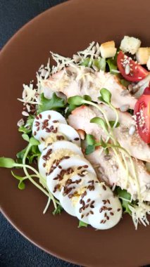 İçinde tavuk, parmesan peyniri, domates, kızarmış ekmek, marul yaprağı, keten tohumu, ayçiçeği ve susam tohumları olan bir kâse dolusu sezar salatası.