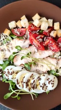 İçinde tavuk, parmesan peyniri, domates, kızarmış ekmek, marul yaprağı, keten tohumu, ayçiçeği ve susam tohumları olan bir kâse dolusu sezar salatası.