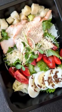 İçinde tavuk, parmesan peyniri, domates, kızarmış ekmek, marul yaprağı, keten tohumu, ayçiçeği ve susam tohumları olan bir kâse dolusu sezar salatası.