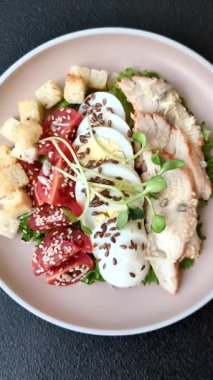 İçinde tavuk, parmesan peyniri, domates, kızarmış ekmek, marul yaprağı, keten tohumu, ayçiçeği ve susam tohumları olan bir kâse dolusu sezar salatası.