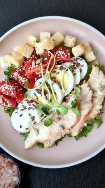 İçinde tavuk, parmesan peyniri, domates, kızarmış ekmek, marul yaprağı, keten tohumu, ayçiçeği ve susam tohumları olan bir kâse dolusu sezar salatası.