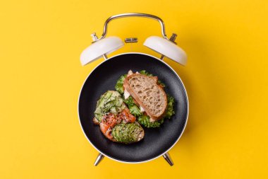 Tost, avokado ve domatesli kahvaltı sandviçi. Kaliteli çalar saatin kadranı yerine tabak konsepti olarak kahvaltı.