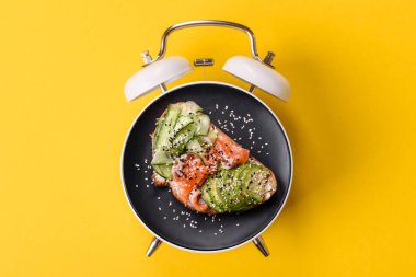 Tost, avokado ve domatesli kahvaltı sandviçi. Kaliteli çalar saatin kadranı yerine tabak konsepti olarak kahvaltı.
