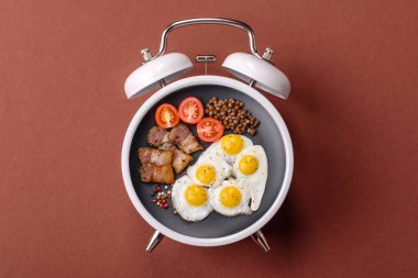 Pastırmalı, sosisli ve sebzeli sahanda yumurta. Kaliteli bir çalar saatin üzerindeki tabak şeklinde kahvaltı.