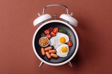 Pastırmalı, sosisli ve sebzeli sahanda yumurta. Kaliteli bir çalar saatin üzerindeki tabak şeklinde kahvaltı.