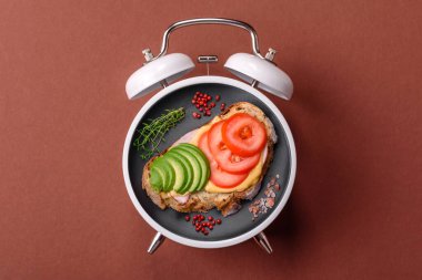 Tost, avokado ve domatesli kahvaltı sandviçi. Kaliteli çalar saatin kadranı yerine tabak konsepti olarak kahvaltı.
