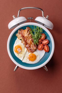 Pastırmalı, sosisli ve sebzeli sahanda yumurta. Kaliteli bir çalar saatin üzerindeki tabak şeklinde kahvaltı.
