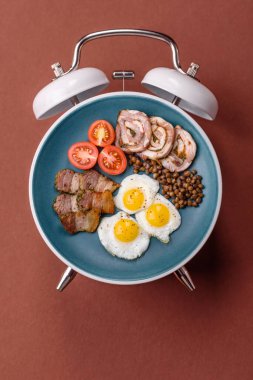 Pastırmalı, sosisli ve sebzeli sahanda yumurta. Kaliteli bir çalar saatin üzerindeki tabak şeklinde kahvaltı.