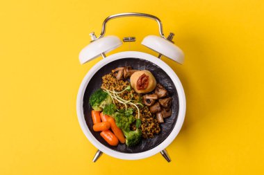 Çalar saatin arka planında kinoalı, sebzeli, etli ve yumurtalı vejetaryen salatası ya da kase. Vejetaryen yemeği yemek için kavramsal geçmiş zamanı