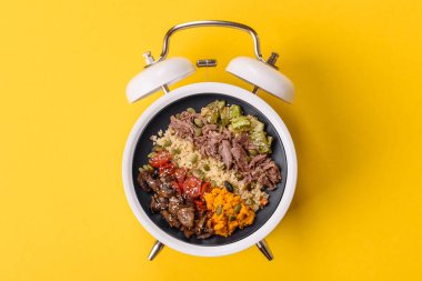 Çalar saatin arka planında kinoalı, sebzeli, etli ve yumurtalı vejetaryen salatası ya da kase. Vejetaryen yemeği yemek için kavramsal geçmiş zamanı