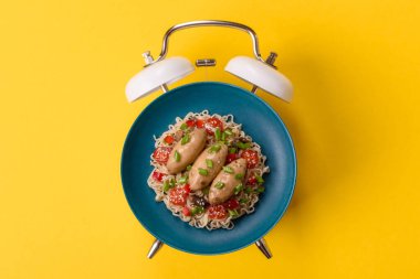 Çalar saatin arka planında et, sos ve sebzeli İtalyan makarnası. Makarna yemek için kavramsal arka plan zamanı