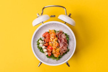 Tavuklu Sezar salatası, kızarmış ekmek, domates ve tohumlu yumurta. Kaliteli çalar saatin kadranı yerine tabak konsepti olarak kahvaltı.