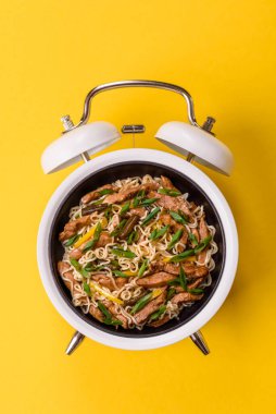 Çalar saatin arka planında et, sos ve sebzeli İtalyan makarnası. Makarna yemek için kavramsal arka plan zamanı