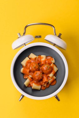 Çalar saatin arka planında et, sos ve sebzeli İtalyan makarnası. Makarna yemek için kavramsal arka plan zamanı