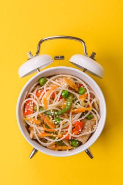 Çalar saatin arka planında et, sos ve sebzeli İtalyan makarnası. Makarna yemek için kavramsal arka plan zamanı