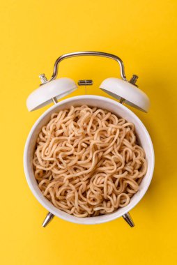 Çalar saatin arka planında et, sos ve sebzeli İtalyan makarnası. Makarna yemek için kavramsal arka plan zamanı