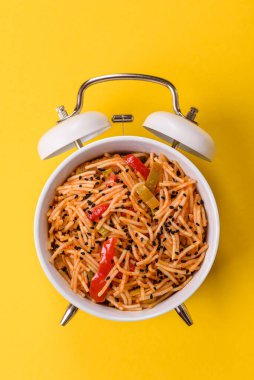 Çalar saatin arka planında et, sos ve sebzeli İtalyan makarnası. Makarna yemek için kavramsal arka plan zamanı