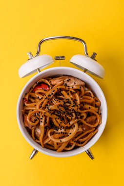 Çalar saatin arka planında et, sos ve sebzeli İtalyan makarnası. Makarna yemek için kavramsal arka plan zamanı