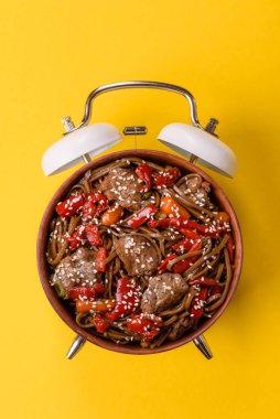 Çalar saatin arka planında et, sos ve sebzeli İtalyan makarnası. Makarna yemek için kavramsal arka plan zamanı