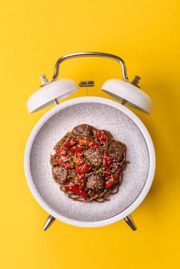 Çalar saatin arka planında et, sos ve sebzeli İtalyan makarnası. Makarna yemek için kavramsal arka plan zamanı