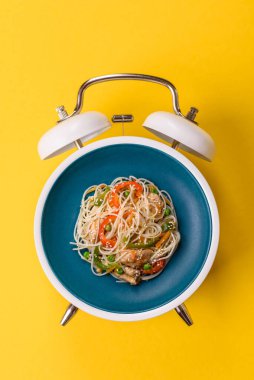 Çalar saatin arka planında et, sos ve sebzeli İtalyan makarnası. Makarna yemek için kavramsal arka plan zamanı