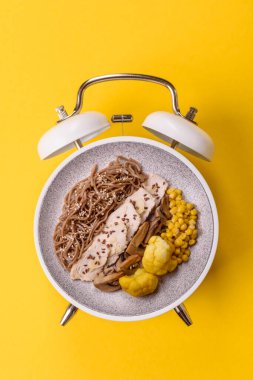 Çalar saatin arka planında et, sos ve sebzeli İtalyan makarnası. Makarna yemek için kavramsal arka plan zamanı