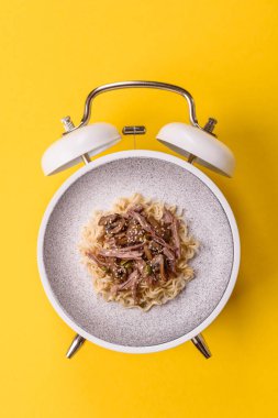 Çalar saatin arka planında et, sos ve sebzeli İtalyan makarnası. Makarna yemek için kavramsal arka plan zamanı